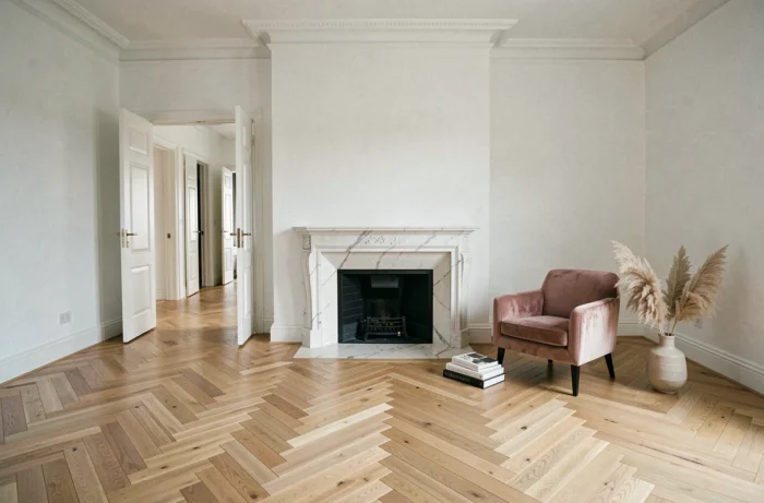 Salon rénové avec parquet en chevrons, cheminée en marbre et fauteuil vintage dans un appartement idéal à décorer
